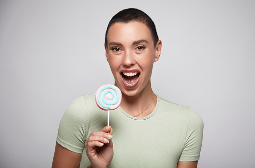 Portrait of a short-haired woman laughing with happiness as she shows her candy to the public.