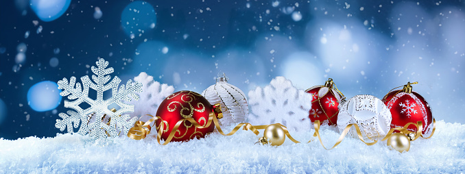 Beautiful Christmas panoramic background with snowflakes and christmas red and white balls in snow against the evening blue sky and snowfall. New Year congratulatory banner.
