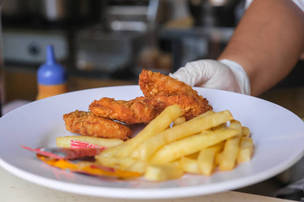Close-up shot of unrecognizable chef serving fresh chicken nugget and fries