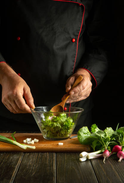 istock The chef mixes lettuce leaves in a bowl with a spoon. Working environment on a restaurant kitchen table. Delicious salad with fresh vegetables by the hands of the cook 1563507561