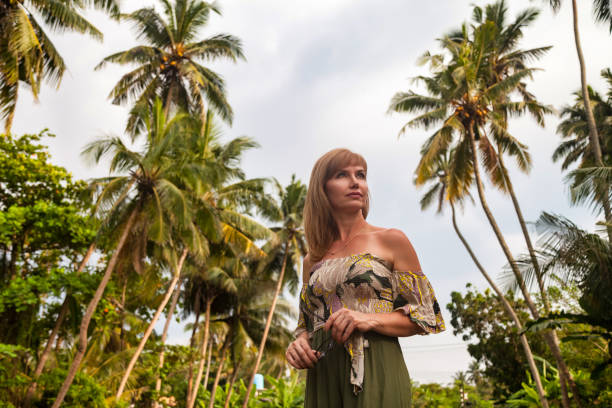 Middle aged lady at tropical jungles background, looking away. Smiling adult woman 50 year old in nature Sri Lanka in tropics with green palm trees. Travel summer vacation concept. Copy ad text space señora de mediana edad en el fondo de las selvas tropicales, mirando hacia otro lado. sonriente mujer adulta de 50 años en la naturaleza de sri lanka en los trópicos con palmeras verdes. concepto de vacaciones de verano de viaje. copiar el espacio de te