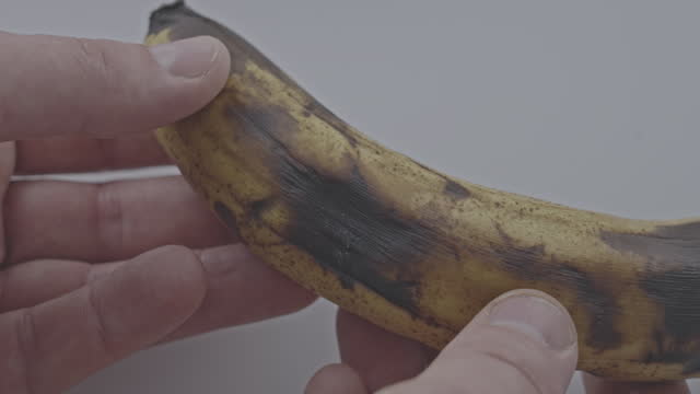 Human hand examines almost rotten banana on home table