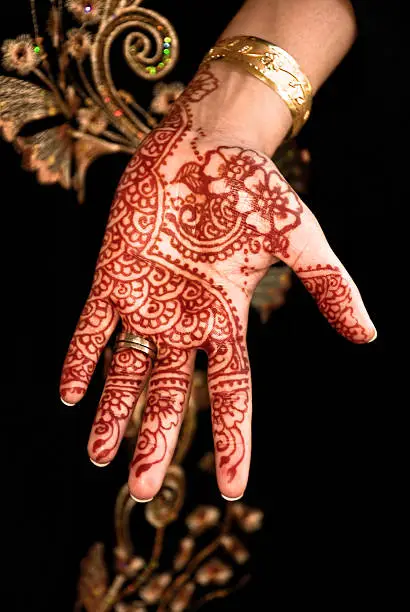 Henna, mehendi on a bride's hand. A traditional custom in the Asian and Arab world. Often the bride to be has henna paste drawings on her hands as decoration and a beauty feature complimenting the other adornments. Also the Muslim women apply henna for the same reasons on the day of Eid festive-ties. Henna is a not a permanent tattoo so is used as an alternative to tattooing.  Black dark background. Left hand.
