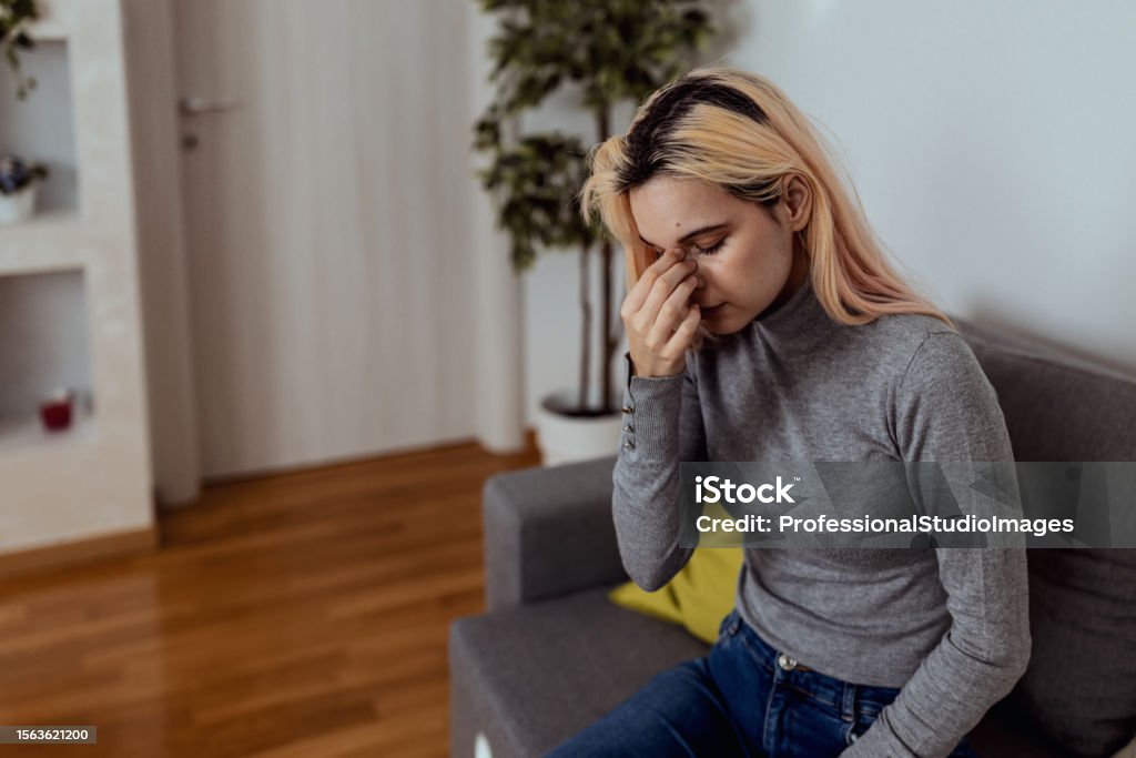 Me and my stuffy nose Poor young Caucasian woman sitting on sofa touching her nose having sinus problems Paranasal Sinus Stock Photo