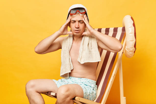 istock Sick shirtless man sitting on deck chair isolated over yellow background spending lots hours sunbathing suffering headache has insolation. 1563656609