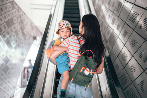 Mother And son  carrying rucksack while riding an escalator, commuting to school