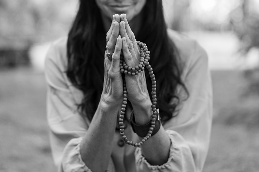 A mindful woman is holding hands in a namaste position while practicing breathing outdoors.