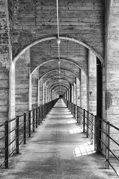 Black & White vertical perspective shot of a pedestrian passerelle under the concrete arcades of an old railway bridge above it