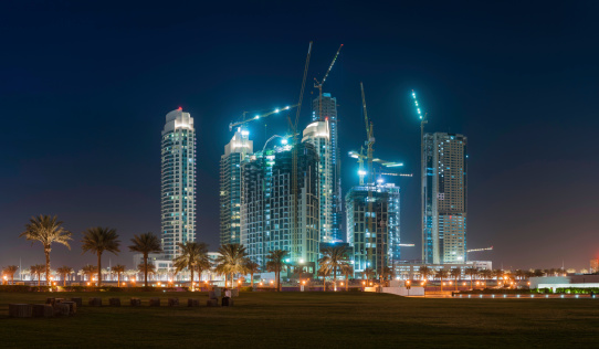 Highrise apartment blocks, office buildings and construction cranes illuminated against the dusk desert skies of Dubai, UAE. ProPhoto RGB profile for maximum color fidelity and gamut.