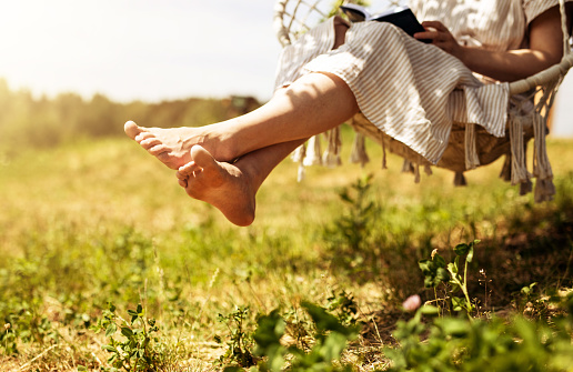 Women legs, barefoot girl sitting on swings in nature, outdoor on summer holiday.