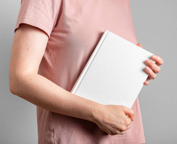 istock Student hand holding book mockup, hardcover, white blank cover mock-up 1563828792