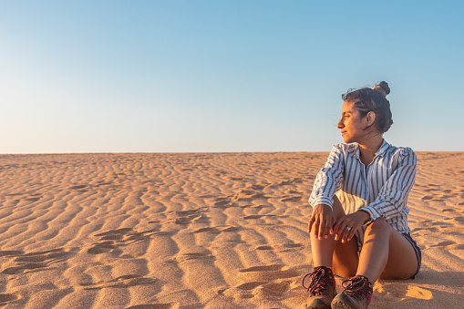 Captivating high desert sunset: Latina woman sitting, embracing the warm glow, surrounded by majestic dunes in the Guajira desert