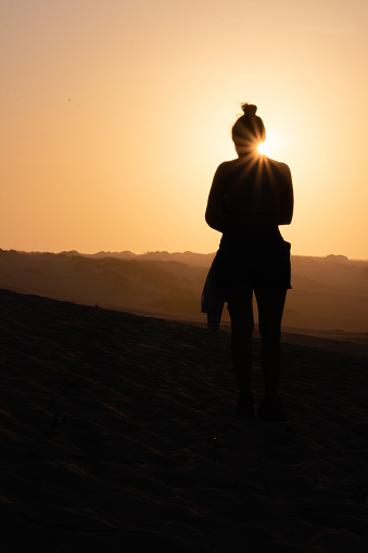 Silhouette of a woman walking on desert dunes, with the rising sun creating a stunning backdrop. Serene beauty at sunset