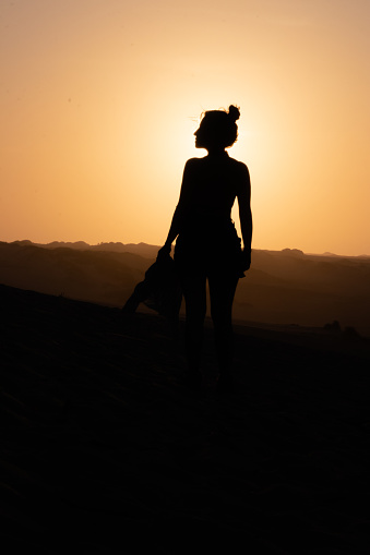Woman's silhouette gracefully walking on dunes as the sun emerges like a rising star behind her shoulder