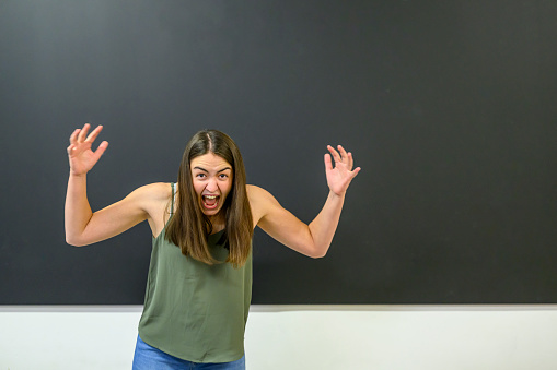 Furious shouting female instructor standing wildly gesticulating at the blackboard in a classroom