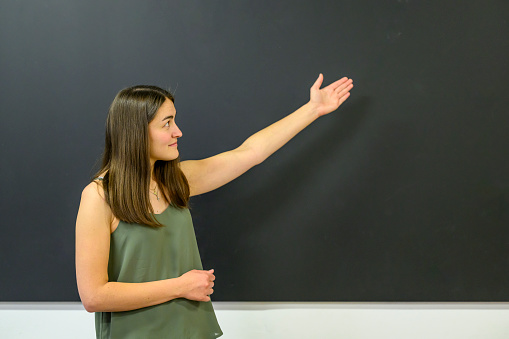 Happy smiling female instructor showing something at the blackboard in a classroom