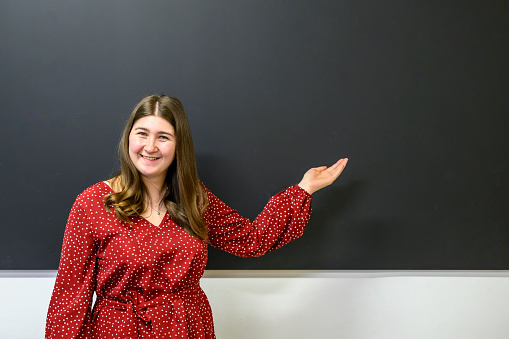 Happy smiling female instructor pointing at something at the blackboard in a classroom