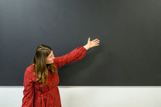 istock Smiling teacher showing something at the blackboard 1563842100