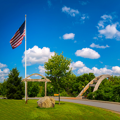 Houlton Riverfront Park in Aroostook County, Northern Maine on a summer day with the American Flag waving in the wind and the view of arching Gateway Crossing Bridge