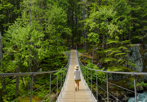 A little girl in a straw hat walks on the old suspension bridge