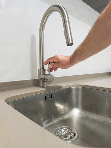 Male hand closing the kitchen sink tap. Selective focus