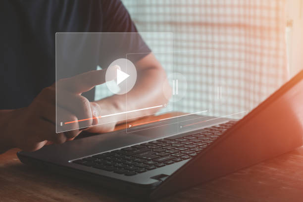 istock streaming online, watching video on internet hologram concept. Video on demand technology with person touching play button on virtual screen to watch online VDO streaming of movie or TV. 1563986683
