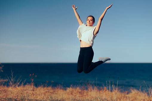 Young happy woman having fun while jumping with her eyes closed during summer dusk on the beach. Copy space.