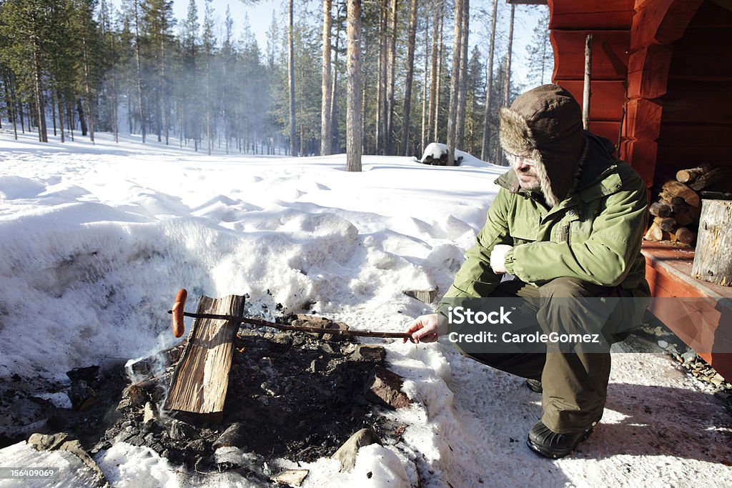 Uomo cucinare salsicce su un fuoco all'aperto - Foto stock royalty-free di Cucinare
