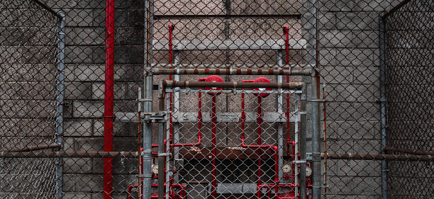 Wire fence surrounding some red pipelines.