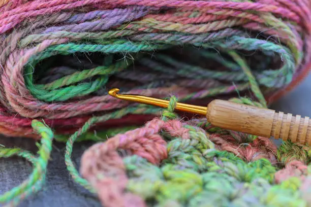 Closeup detail of crochet work with a colourful skein of organic natural handspun and handdyed merino sheep wool, silk, linnen mix yarn fleece, spun on a traditional spinning wheel