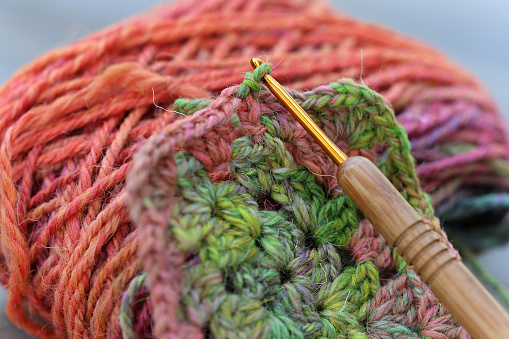 Closeup detail of crochet work with a colourful skein of organic natural handspun and handdyed merino sheep wool, silk, linnen mix yarn fleece, spun on a traditional spinning wheel