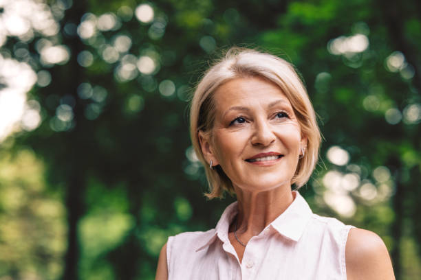 A Happy Beautiful Blonde Woman Looking Away While Relaxing In Nature A portrait of a smiling senior Caucasian female contemplating while standing outdoors. older blonde woman stock pictures, royalty-free photos & images