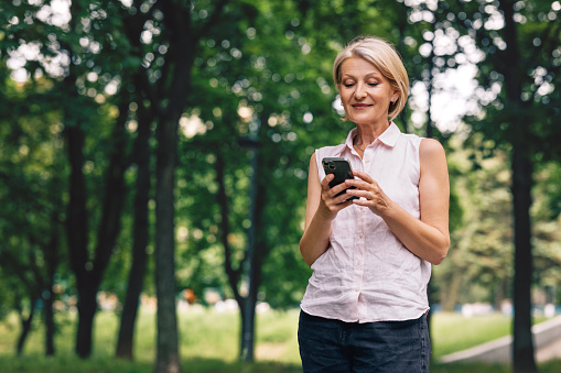 A smiling senior Caucasian female using her smartphone while standing outdoors.