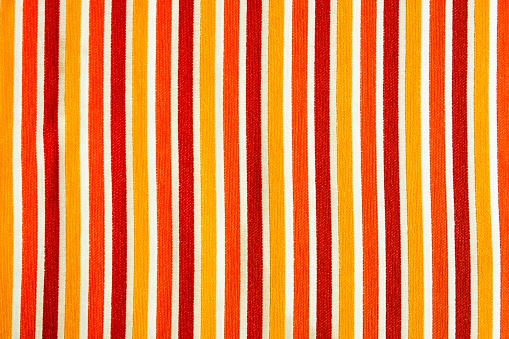 Vertical stripes of yellow, orange and red between white color from weave craft design on cotton fabric for cozy couch cover pattern textured background