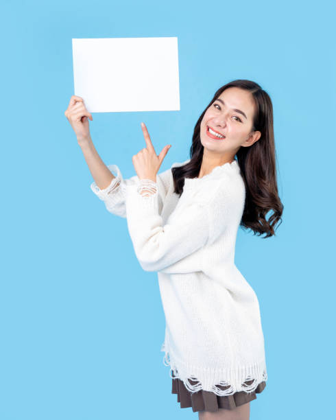 istock Your text here. Young excited woman holding empty blank board. Colorful studio portrait with light blue background. Woman holding blank empty banner pointing finger to one self smiling happy and proud 1564327551