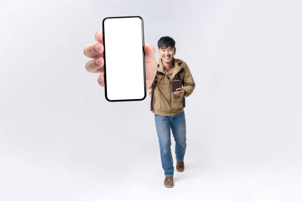 istock Full length happy Asian man backpacker walking with showing cellphone blank screen with empty space for mobile app on screen. Isolated in studio white background. Creative collage. 1564405862