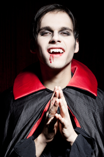 Male vampire with folded hand seems to look forward to his next prey. Dried blood is on the side of his mouth.