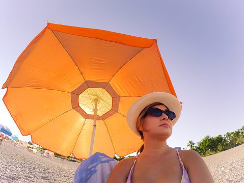 Woman enjoying vacation under orange beach umbrella.