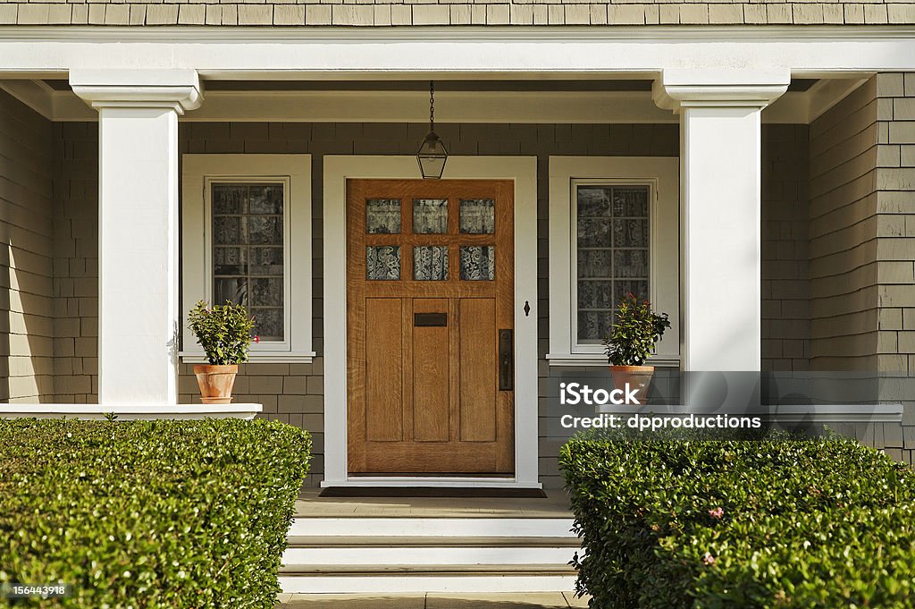 Wooden Front Door A concrete walkway bordered with hedged shrubs leads to the front door of a home. There are windows on either side of the door. Horizontal shot. Front Door Stock Photo