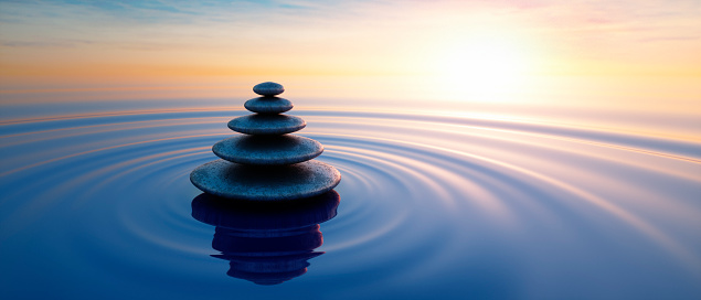 Stack of dark stones podium in calm ocean with evening sun with horizon - tranquil scenery