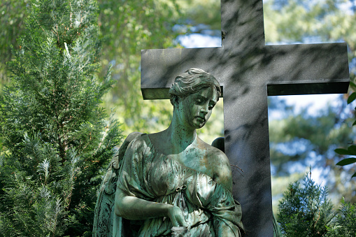 Old copper angel statue and a stone cross in a cemetery