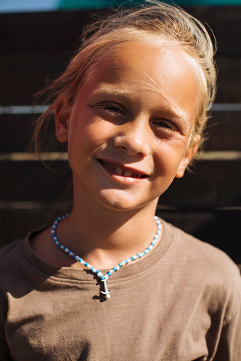 A young blond boy poses for a portrait photo while wearing a necklace on vacation