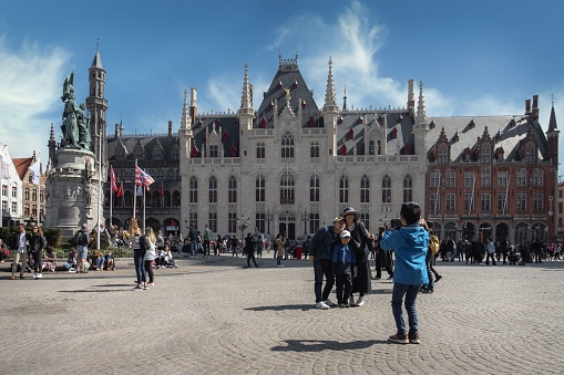 BRUGUES, Belgium – July 08, 2023: A group of people in Bruges, Belgium, gathered in a city square surrounded by tall, historical buildings