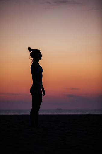 A young woman stands on the beach at dusk