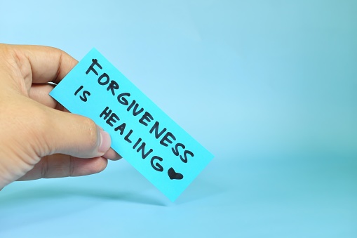 Forgiveness is healing concept. Hand holding a blue paper reminder message note.