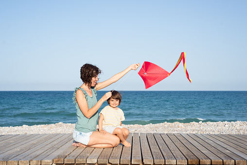 Mother and daughter playing with a kite at a pebble beach.