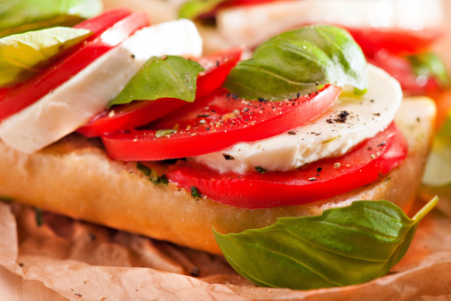 Closeup of a fresh sandwich with mozzarella, tomatoes and basil seasoned with black pepper