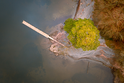 Aerial birds eye view of long wooden jetty on shoreline of island in the Lake District, UK.