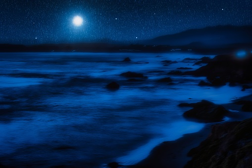 composition of a mysterious view of the pacific ocean and waves in long exposure at night with moon and shooting stars