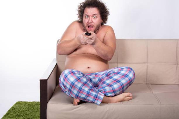 istock Funny fat man watching tv at home. 1564637658